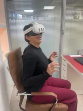 Someone in a headset seated in an office chair, both hands lifted in front of them, beside a glazed partition in a second consulting room.